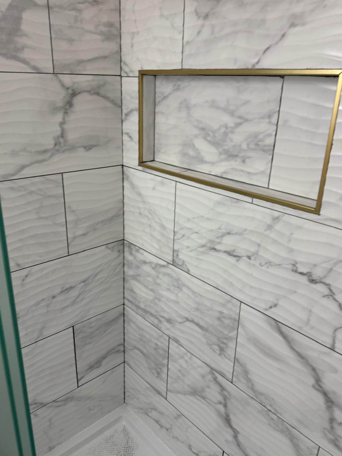 Gold-trim shower niche in marble-look wave tile